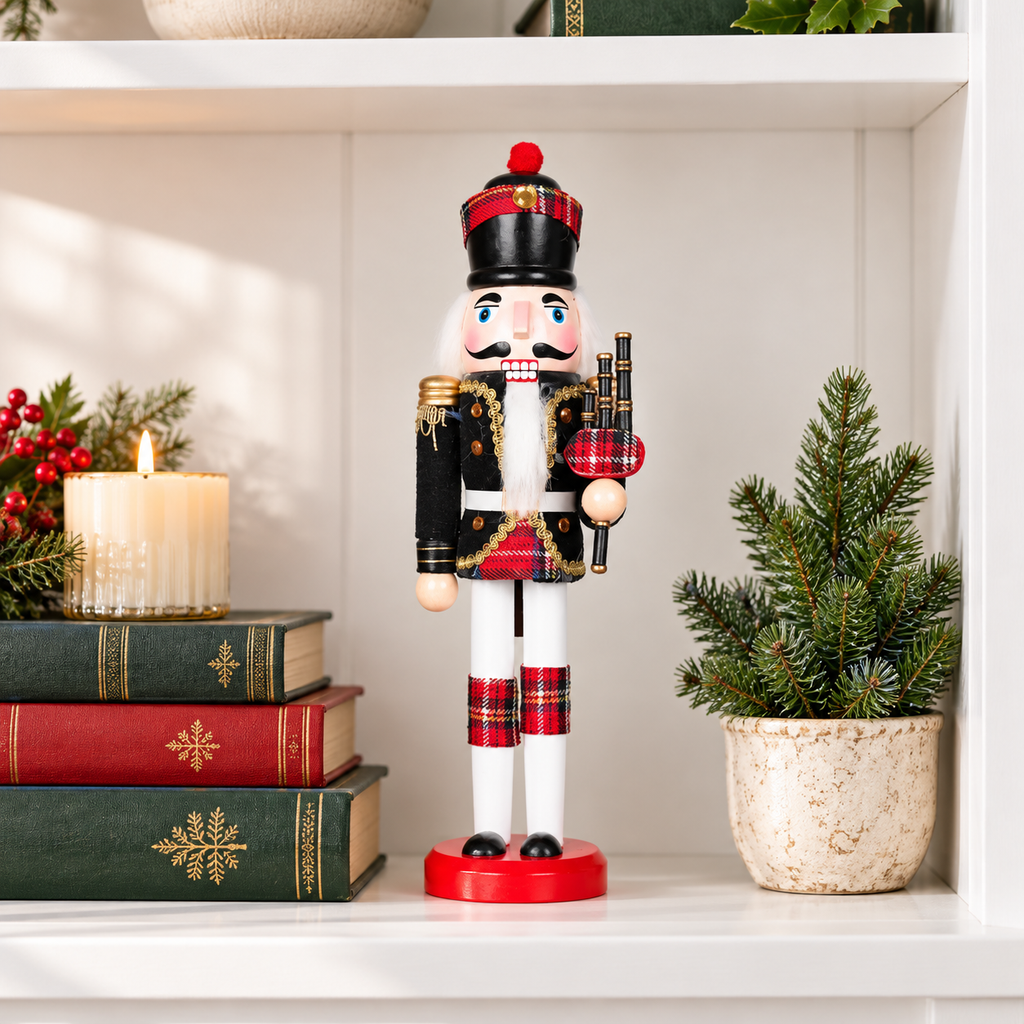 Scottish bagpiper nutcracker on a white shelf beside green and red books, a candle and a small evergreen to show its 12 inch size