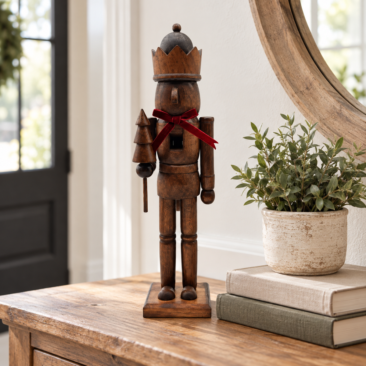 Wooden nutcracker with red bow styled on an entryway table with books and greenery