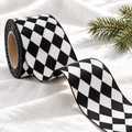 Roll of 1.5 inch black and white harlequin diamond ribbon partly unrolled on white linen with a pine sprig