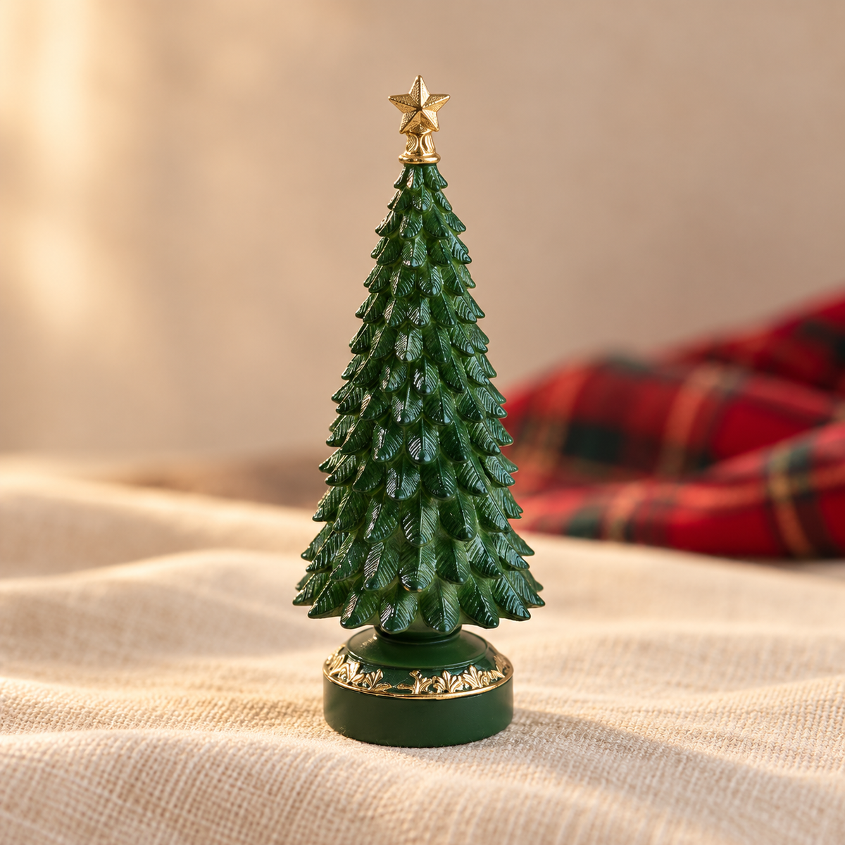 Green resin tabletop Christmas tree with gold star on cream linen beside red tartan fabric