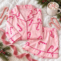 Pink candy cane satin pajama shirt and shorts folded flat with candy canes, pine and a mug of cocoa