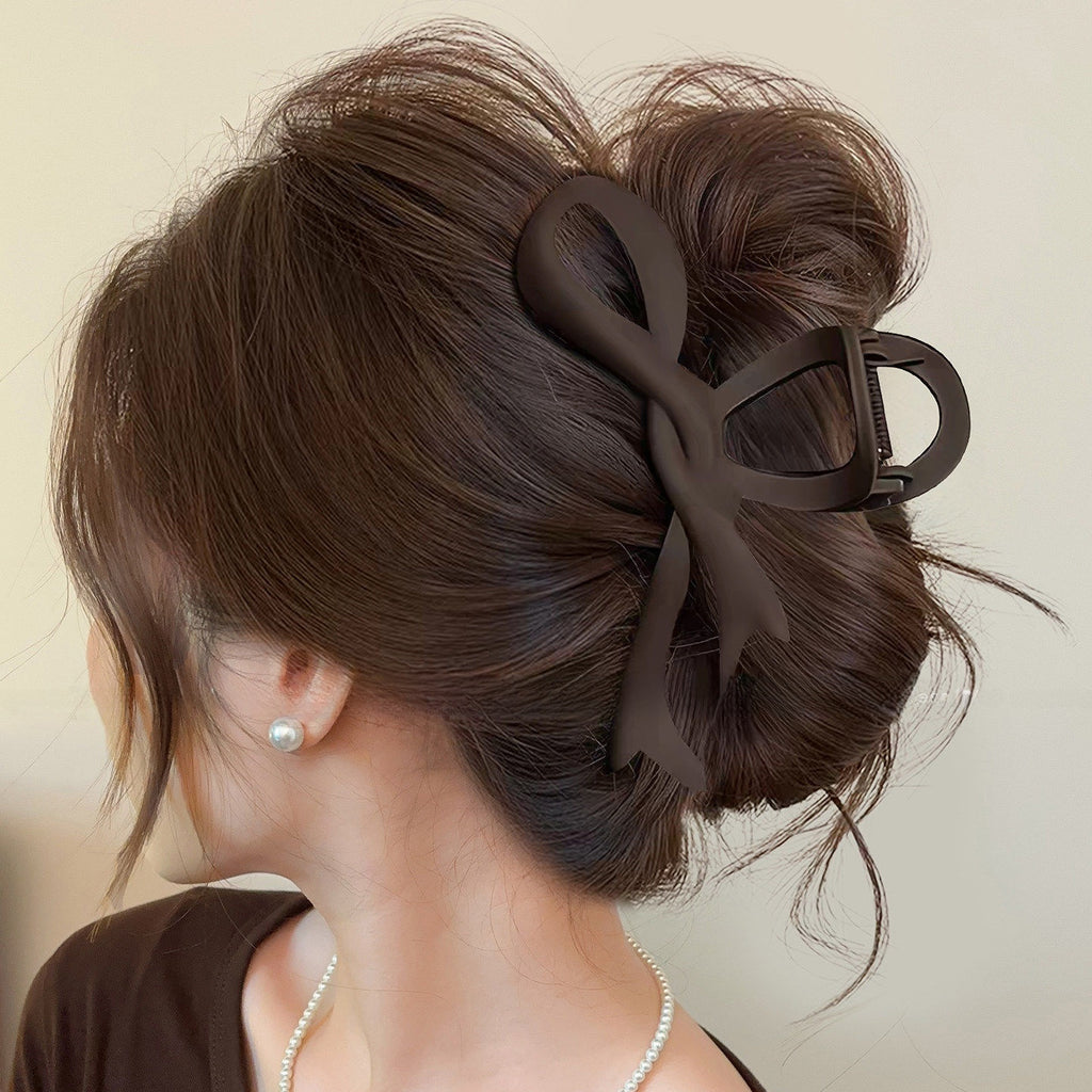 Matte dark coffee brown bow claw clip holding a messy bun