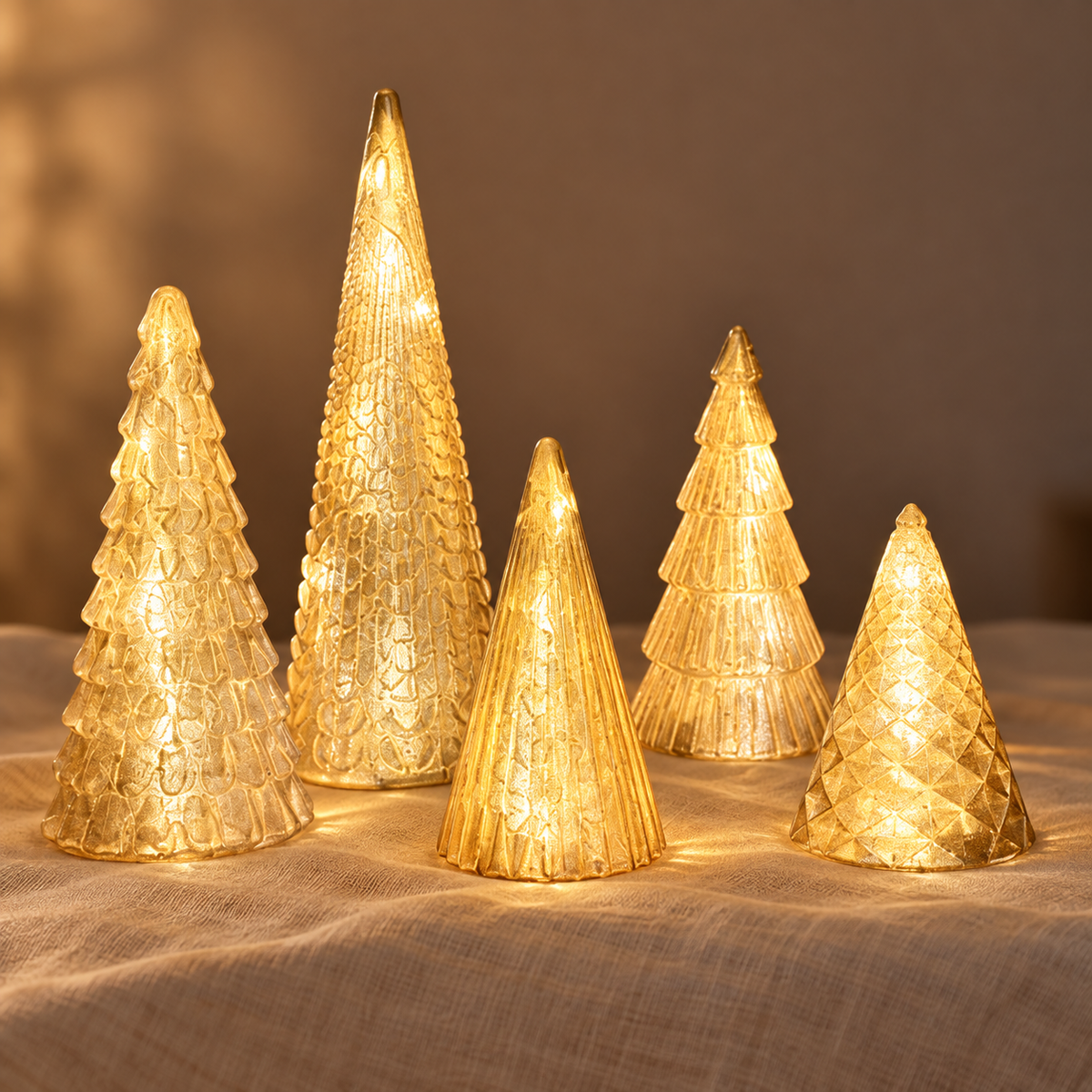 Set of 5 gold lighted tabletop Christmas trees glowing warm white on cream linen