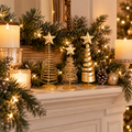 Three gold metal tabletop Christmas trees on a fireplace mantel with garland, candles and lights