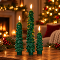 Set of 3 green wax Christmas tree LED flameless candles glowing on a wooden table in a cozy living room by the fireplace