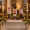 Set of 3 hand-painted wooden nutcrackers on a white fireplace mantel with pine garland, twinkle lights and gold candlesticks