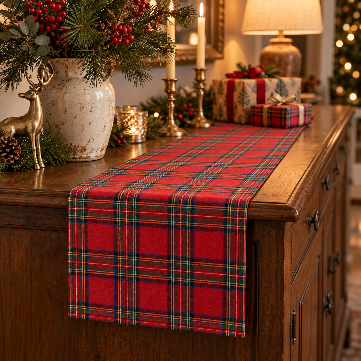 Red tartan Christmas table runner on a wooden sideboard with a lamp, brass candlesticks, and wrapped gifts