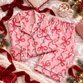 Pink bow print satin pajama top and pants folded flat with red ribbon, pine and cocoa